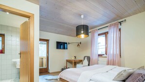 A bedroom with a wooden bed, a TV, a desk, and a window with curtains.