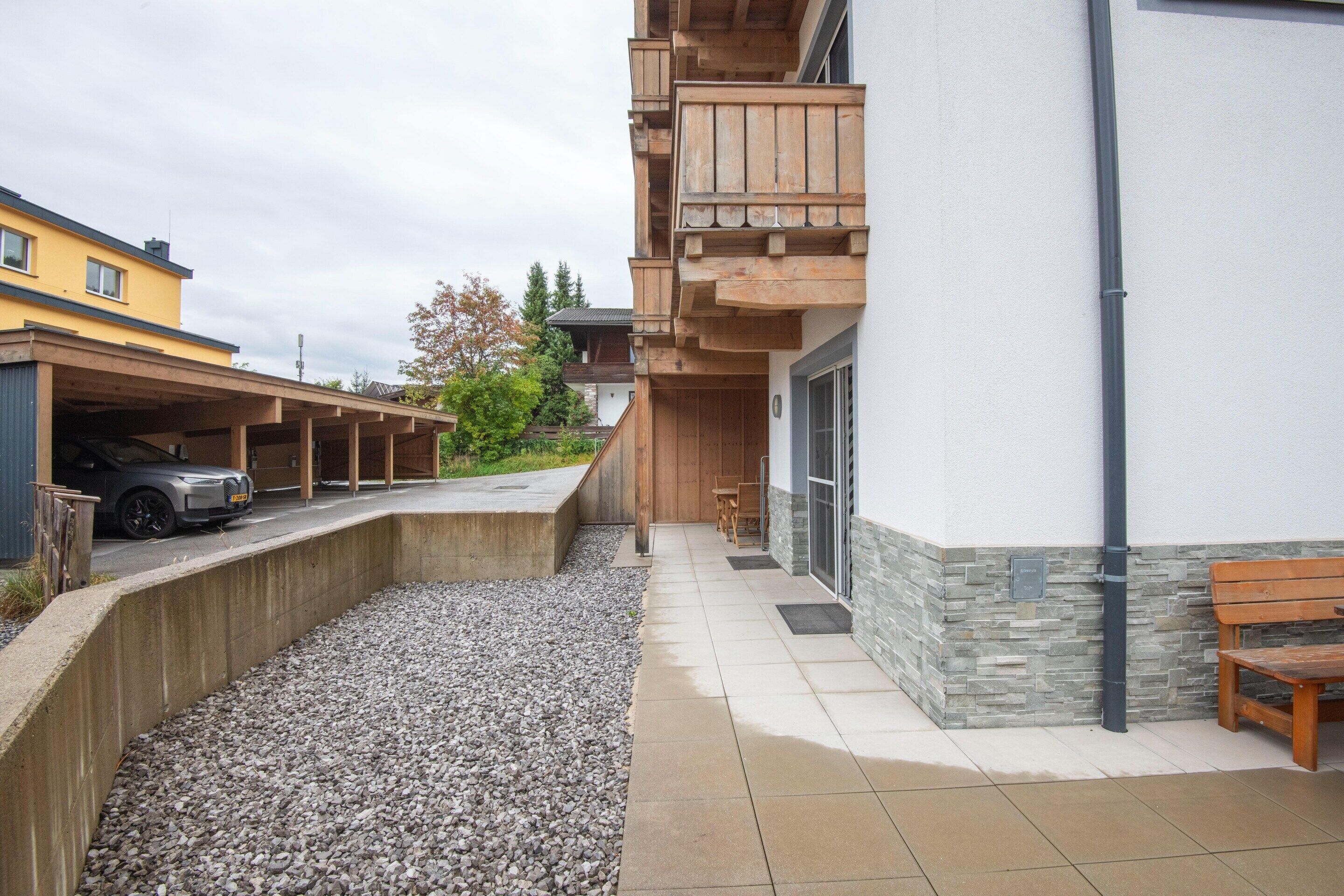 Un edificio con area di parcheggio coperta, un vialetto sterrato e una panchina di legno.
