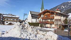 A hotel with a prominent green spire, a large snow pile in front, and a mountain backdrop. - Apartment in Kaltenbach Near Ski Lift (Stumm)