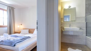 Ein Hotelzimmer mit Bett, Nachttisch, Bad mit Waschbecken, Spiegel und Dusche.