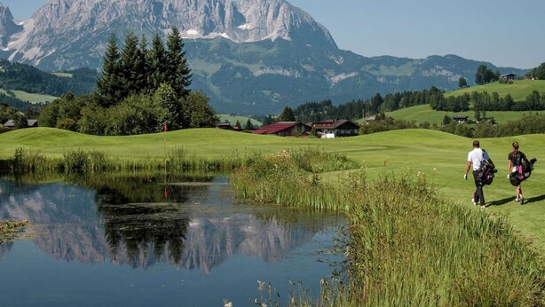 Ein Golfplatz mit Teich, Bäumen und einem Berg im Hintergrund.