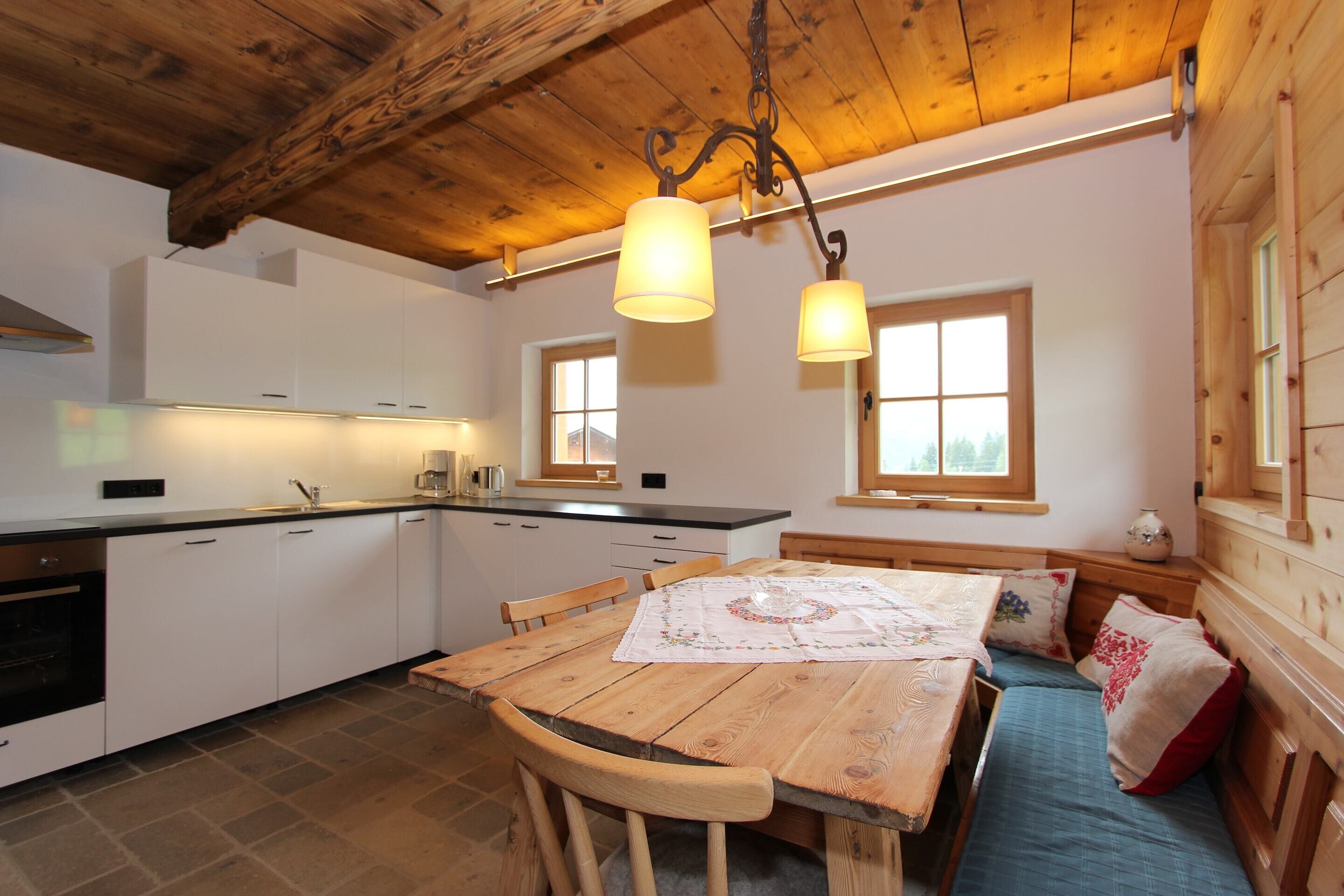A cozy kitchen with wooden beams, white cabinets, and a dining table with a bench.