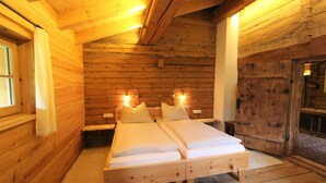 A wooden cabin bedroom with two beds, wooden walls, and a large wooden door. - Cozy Chalet in Sankt Johann in Tirol near Ski Area (Sankt Johann in Tirol)
