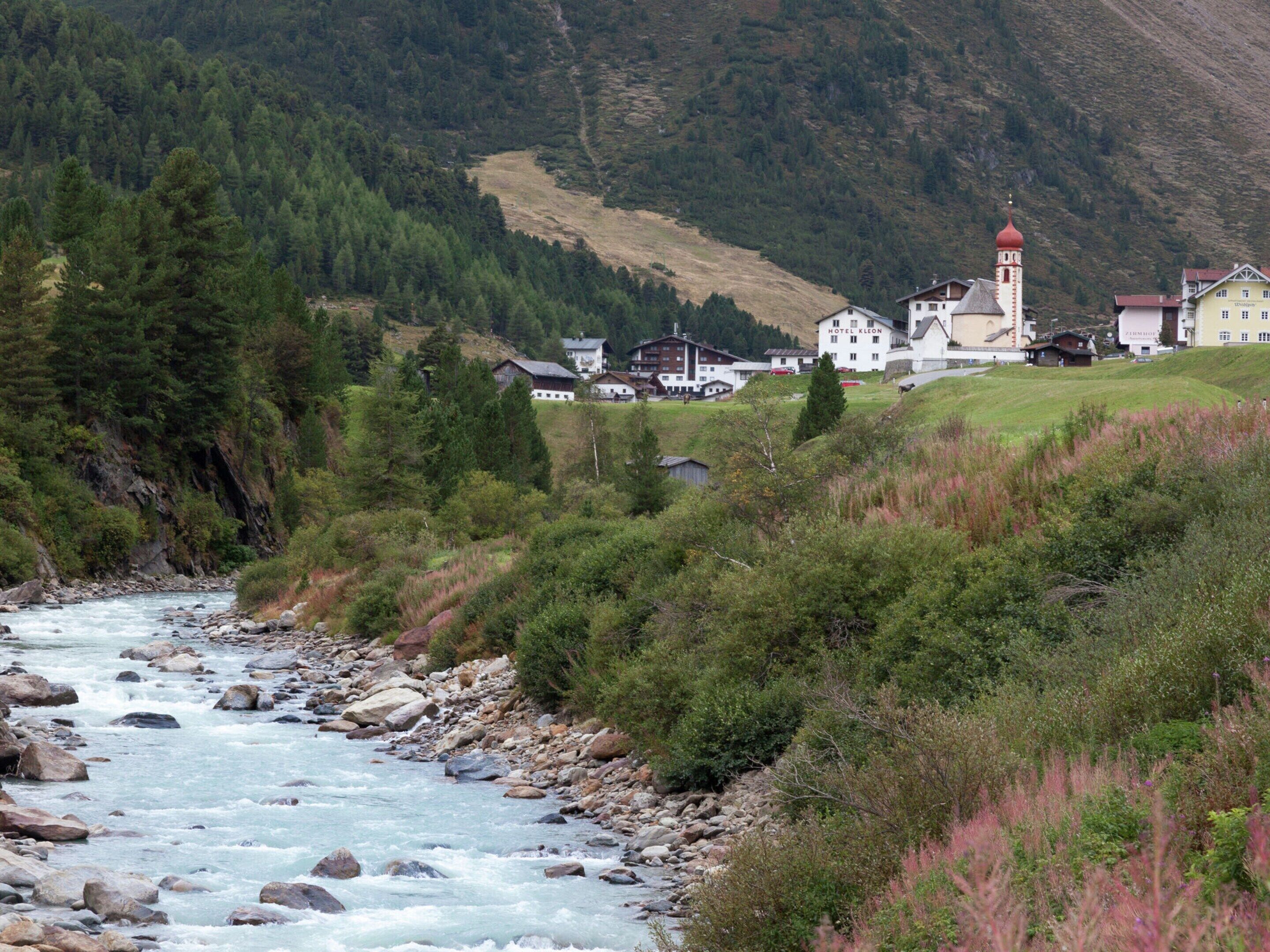 Une rivière traverse une vallée, avec un hôtel et une église en arrière-plan.