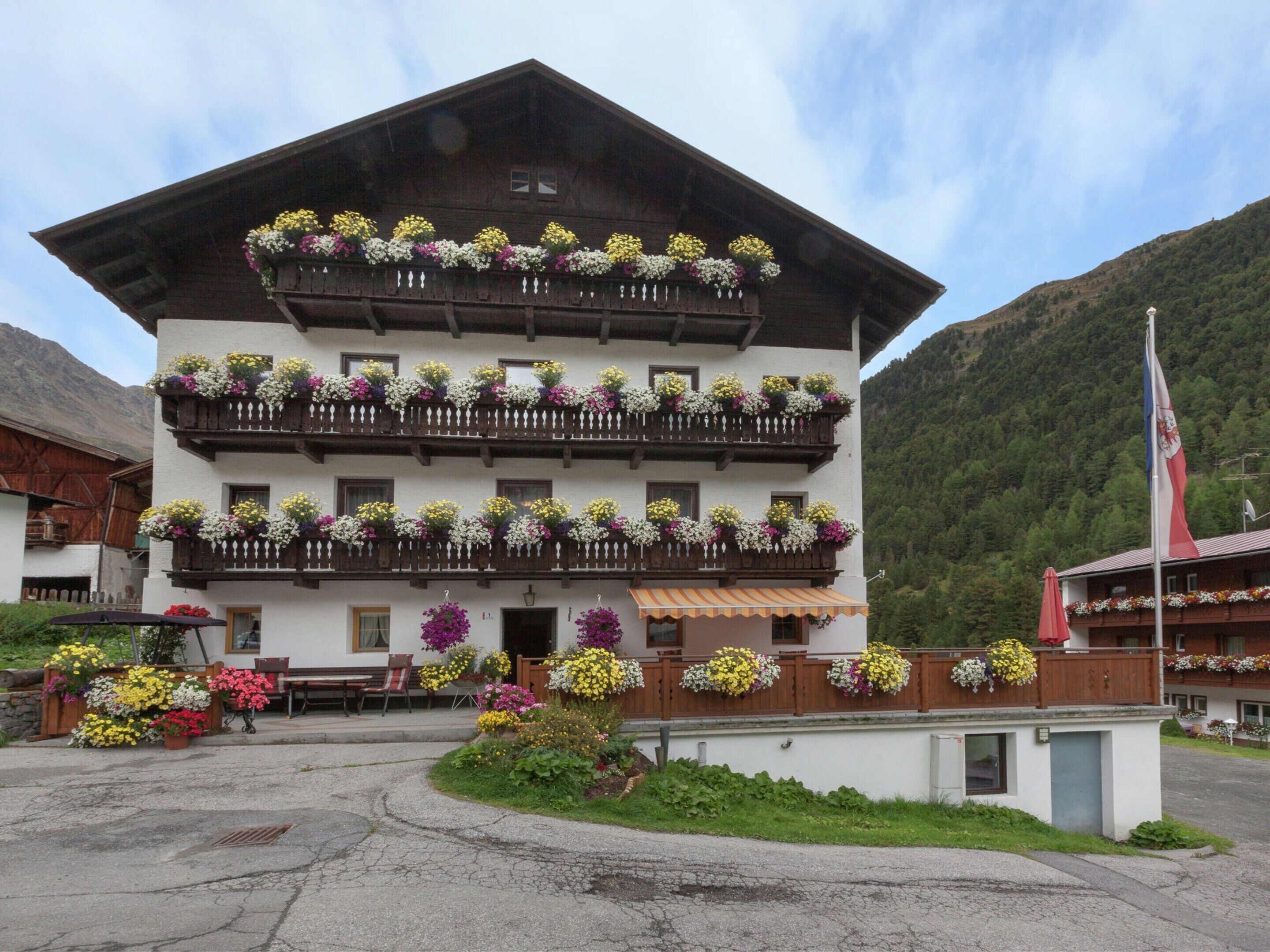 A multi-story building with balconies adorned with flowers, a flag, and a mountainous backdrop.