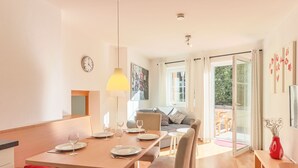 A modern dining area with a wooden table set for four, a sofa, and a view of the outdoors.