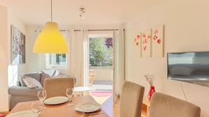 A dining area with a wooden table set for four, a yellow pendant light, and a TV mounted on the wall.