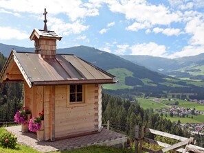 A wooden cabin with a metal roof, a chimney, and a small window. It is surrounded by a wooden fence and has a view of a valley with houses and trees. - Modern Apartment in Brixen im Thale Tyrol With Terrace (Brixen im Thale)