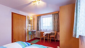 Une chambre d’hôtel avec deux lits, une petite table, une chaise, une fenêtre avec des rideaux, un radiateur et une armoire en bois.