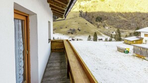 Un balcon doté d’un plancher en bois, offrant une vue sur un paysage enneigé avec des maisons et une colline en arrière-plan.