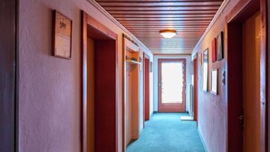 Un couloir avec un plafond recouvert de lambris en bois, un sol moquetté et des portes donnant sur différentes pièces.