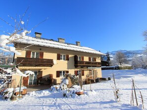 Un chalet à deux étages doté d’un balcon, entouré d’un paysage enneigé et d’arbres.