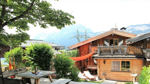 A wooden cabin with a deck, outdoor seating, and a view of mountains. - Chalet in St Johann on Ski Slopes (Sankt Johann in Tirol)