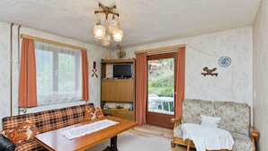 A cozy living room with a sofa, a wooden table, a television on a stand, and a door leading to an outdoor area. - Villa in Piller Near Ski Bus & Lake (Fliess)