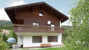 A two-story chalet with a balcony, a satellite dish, and a small outdoor seating area with a bench and chairs. - Villa in Piller Near Ski Bus & Lake (Fliess)