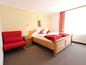 A bedroom with a wooden bed, red chair, and a picture on the wall.