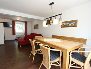 A dining area with a wooden table and wicker chairs, a red sofa, and a television mounted on the wall.