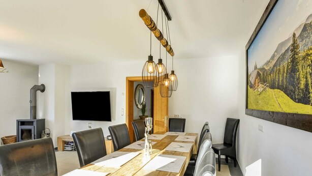 A dining area with a long wooden table, black chairs, and a modern chandelier. - Luxury Holiday Home in Brixen im Thale Near Ski Area (Brixen im Thale)