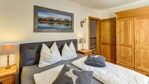 A bedroom with a bed, a nightstand, a lamp, a framed picture, a wooden wardrobe, and a deer head decoration. - Luxury Holiday Home in Brixen im Thale Near Ski Area (Brixen im Thale)