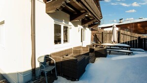 A covered outdoor seating area with wicker furniture, a metal chair, and a wooden table. - Luxury Holiday Home in Brixen im Thale Near Ski Area (Brixen im Thale)