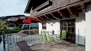 An outdoor seating area with lounge chairs and tables, a stone patio, and a wooden building with a balcony. - Apartment in St. Johann in Tyrol With a Garden (Sankt Johann in Tirol)