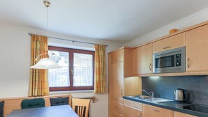 A compact kitchen with wooden cabinets, a built-in microwave, a sink, and a dining area with a table and chairs. - Apartment Brixen Near Ski Lift (Brixen im Thale)