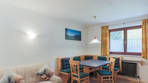 A cozy room with a sofa, a dining table with chairs, a pendant light, a window with curtains, and a radiator. - Apartment Brixen Near Ski Lift (Brixen im Thale)