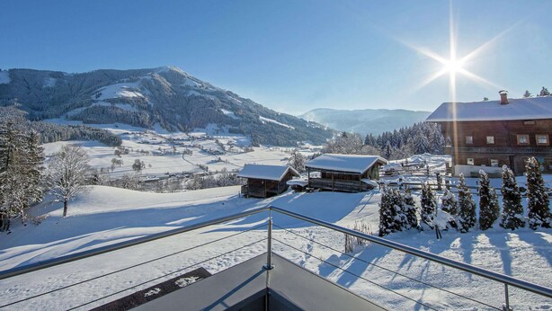 A snow-covered landscape with a building featuring a wooden facade and a sloped roof, likely a hotel or lodge, with a view of the surrounding mountains and a clear sky. - Apartment Brixen Near Ski Lift (Brixen im Thale)