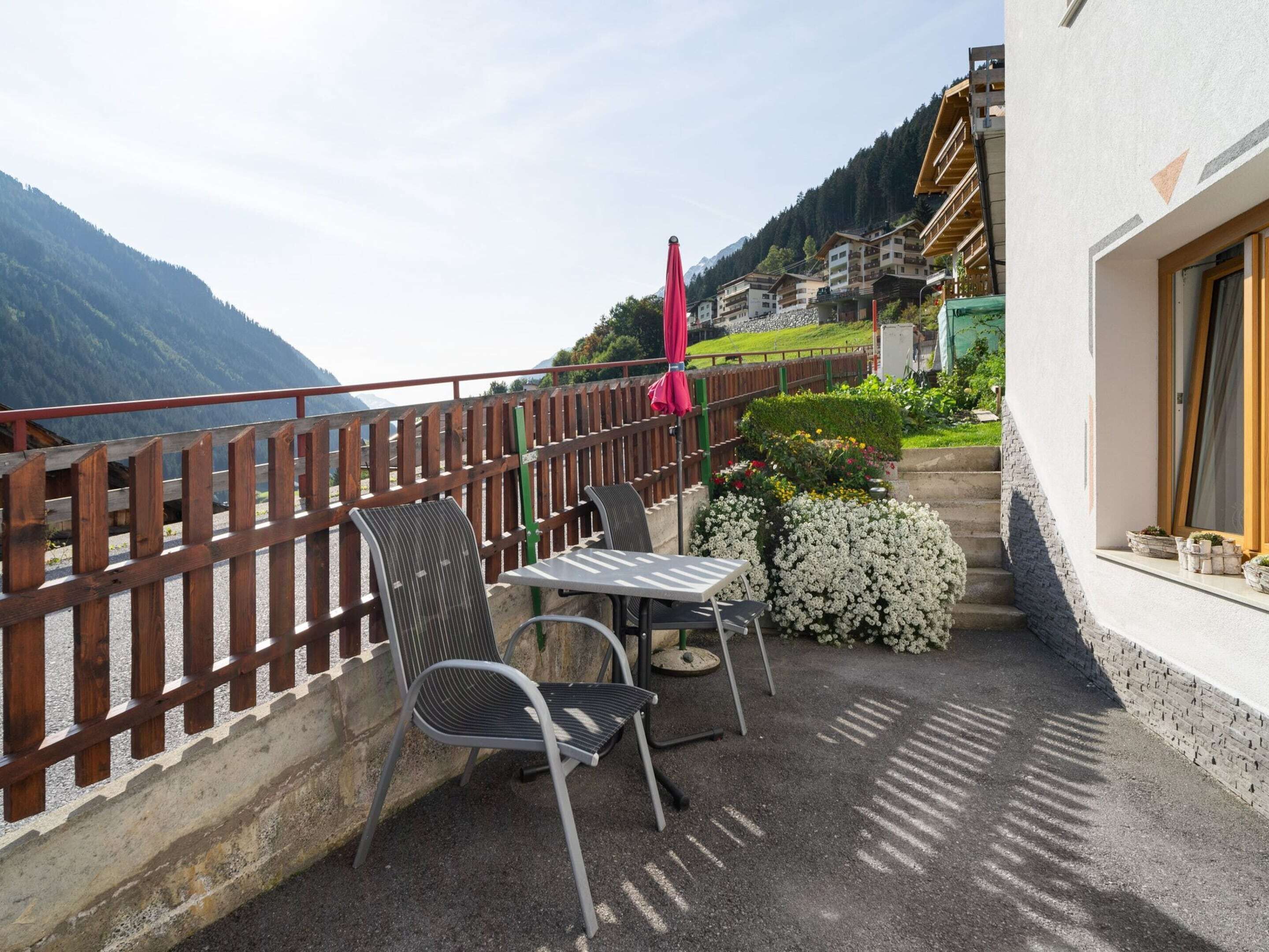 A terrace with a table and two chairs, a wooden fence, and a view of a mountain.