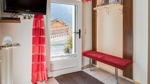 A hotel room with a television, a bench, a door with a view of a wooden cabin, and a shelf with a poster. - Apartment in Kappl Near Ski Lift (Kappl)