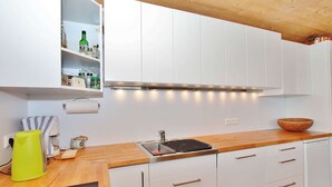 Une cuisine moderne avec des armoires blanches, un plan de travail en bois, un four encastré et un évier en acier inoxydable.