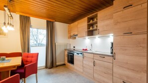 A modern kitchen with wooden cabinets, a built-in oven, and a dining area with red chairs. - Modern Apartment in Kitzbuhel Near Ski Area (Kitzbuhel)
