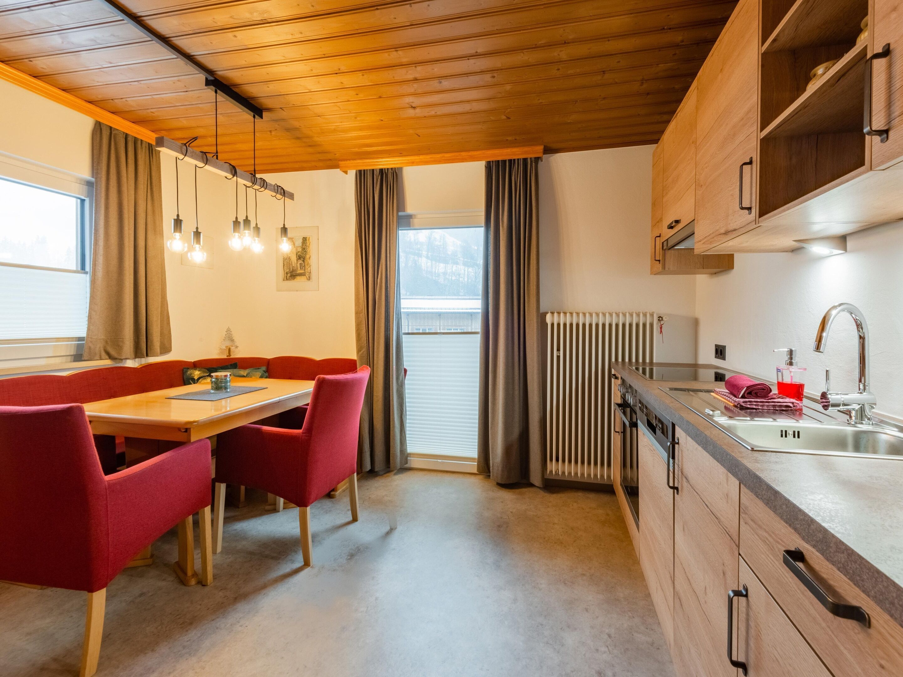 A compact kitchen with wooden cabinets, a dining area with red chairs, and a radiator.