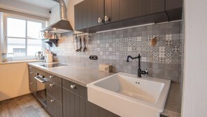 A modern kitchen with dark cabinets, a white sink, and patterned backsplash tiles. - Apartment in Brixen Near Skiwelt Lift (Brixen im Thale)