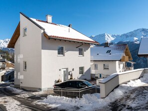 A two-story building with a sloped roof, a car parked in front, and snow on the ground.