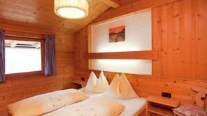 A wooden cabin room with a bed, a bench, and a window with curtains. - Apartment in Waidring Near Ski Slopes (Waidring)