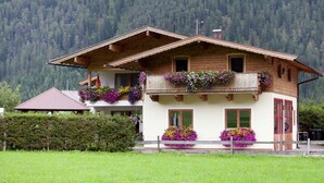 A two-story chalet with wooden balconies adorned with flowers, set against a forested mountain backdrop. - Apartment in Waidring Near Ski Slopes (Waidring)