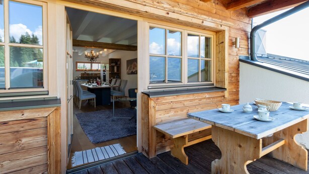 A wooden cabin with a dining area, large windows, and a view of the mountains. - Apartment With Sauna and Ski In/out (Mittersill)