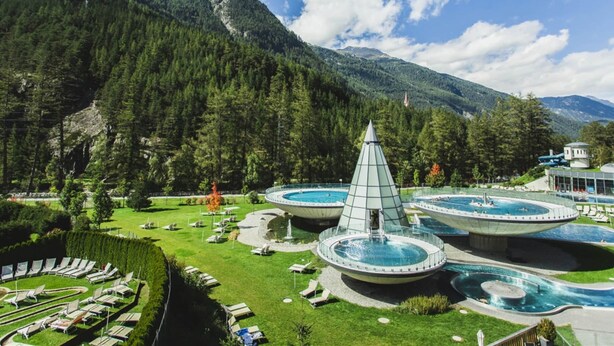 A resort with multiple swimming pools, a central glass pyramid structure, and a mountainous backdrop.