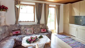 Ein gemütliches Wohnzimmer mit einer sofaartigen Sitzecke im Steinmuster, einem kleinen Tisch mit Blumen und einer Küchenzeile mit weißen Schränken.