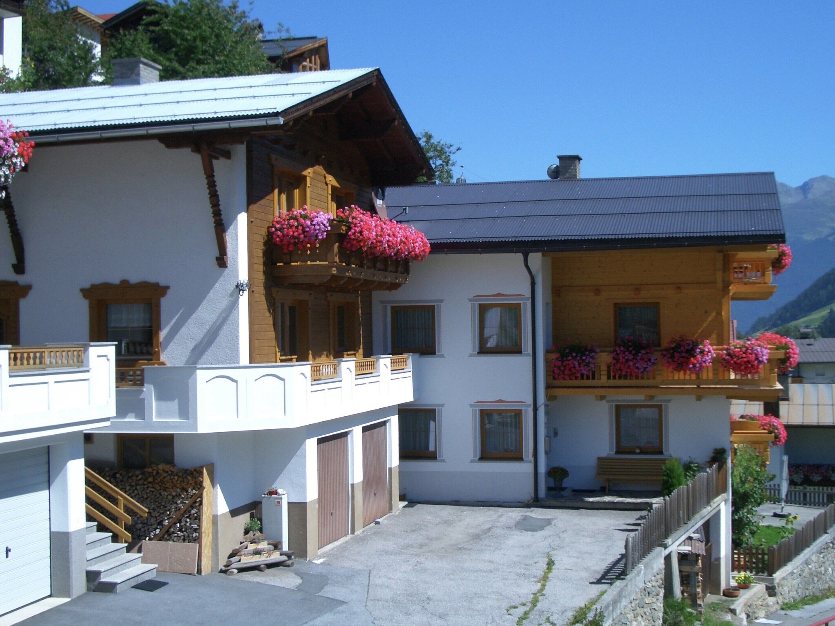 Un chalet tradicional con balcones de madera decorados con flores, una escalera de piedra y vistas despejadas de las montañas circundantes.