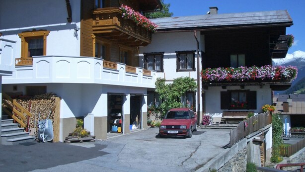 A traditional chalet with a wooden balcony, a red car parked in front, and a mountain backdrop. - Apartment in Kappl Near Ski Lift (Kappl)