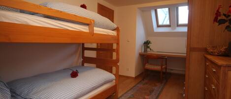 Ein Schlafraum mit Etagenbett, Schreibtisch, Stuhl, kleinem Fenster und Holzschrank.