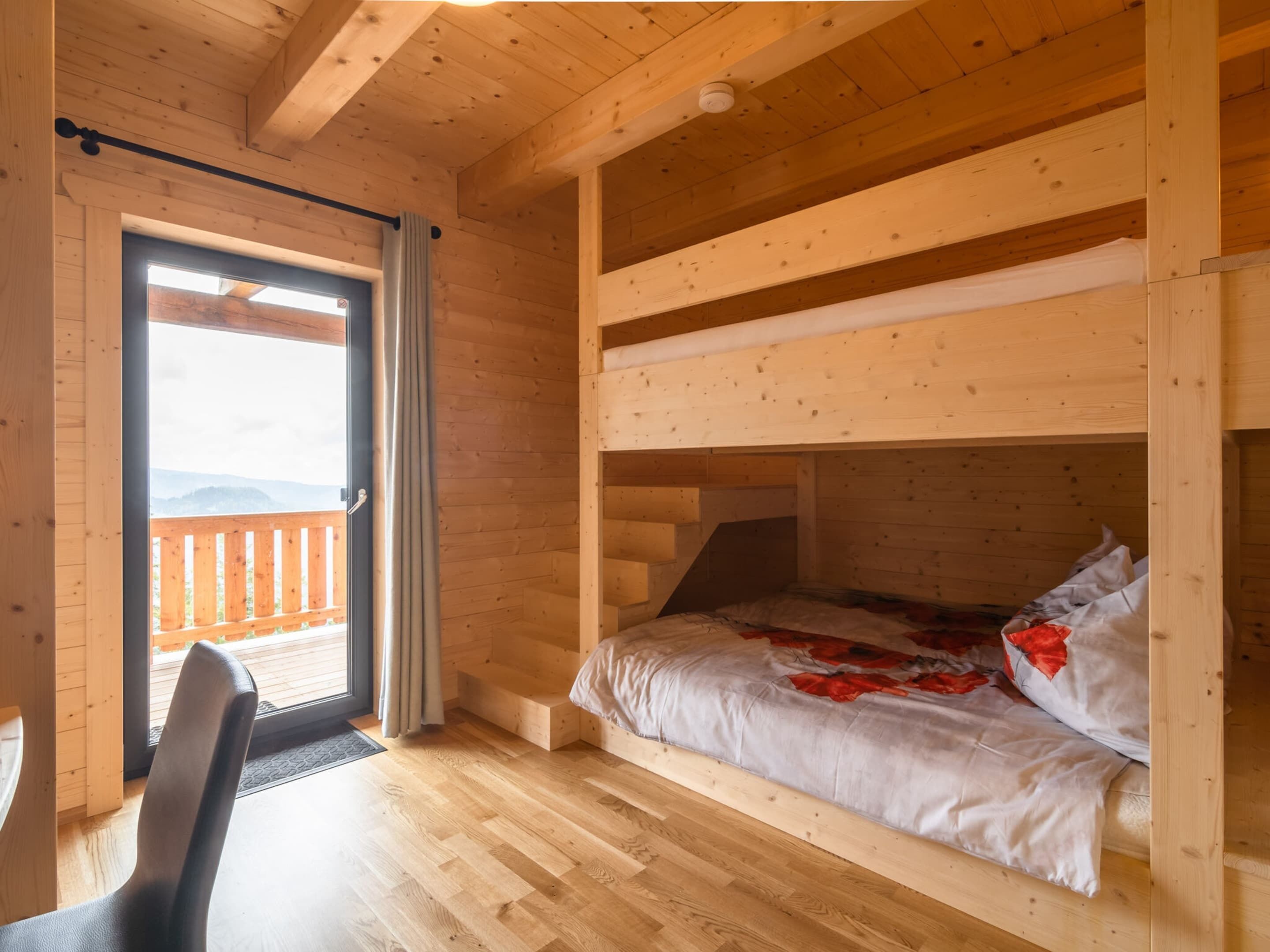 Ein Zimmer in einer Holzhütte mit einem Etagenbett, einem Schreibtisch und Blick auf eine Holzterrasse und Berge.