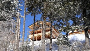 A wooden chalet with multiple balconies, surrounded by snow-covered trees and a clear blue sky. - Chalet in Klippitztorl ski Area With Sauna (Bad Sankt Leonhard im Lavanttal)