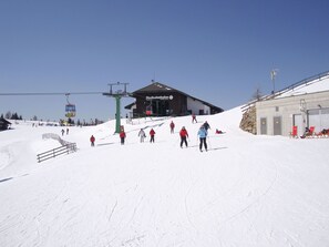 Un centro de esquí con un telesilla, un edificio con la leyenda 'Nockalmbahn' y una ladera cubierta de nieve.