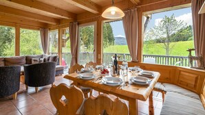 A wooden cabin with a dining area, large windows, and a view of the outdoors. - Wooden Chalet in Styria near Kreischberg Ski Area (Sankt Georgen am Kreischberg)