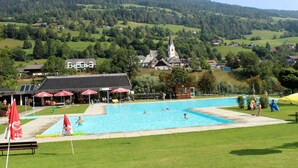 A swimming pool with people, a church, and houses in the background. - Wooden Chalet in Styria near Kreischberg Ski Area (Sankt Georgen am Kreischberg)