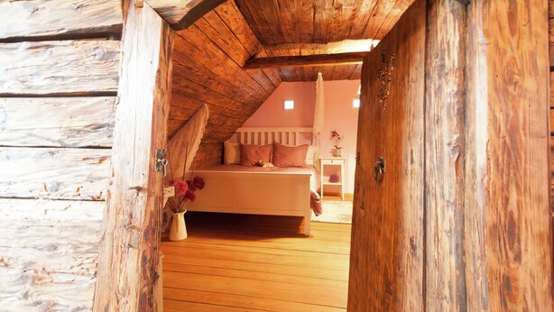 A rustic wooden room with a sloped ceiling, a bed with pillows, a bedside table, and a vase with flowers. - Apartment in Neuhaus Near Petzen Ski Area (Neuhaus)