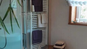 A bathroom with a glass shower enclosure, a towel rack with folded towels, a wooden stool, and a window with blinds. - Apartment in Neuhaus Near Petzen Ski Area (Neuhaus)